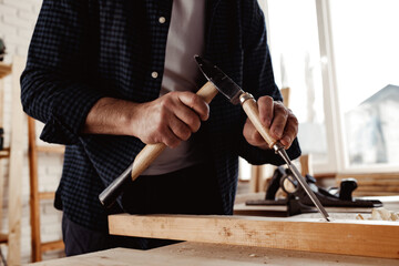 Hands of a carpenter working with chisel and hammer
