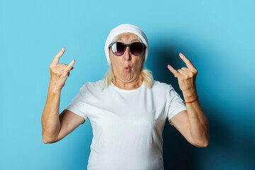 Funny old woman in a hat and glasses, makes a hand gesture on a blue background. Concept cool stylish grandmother, modern style