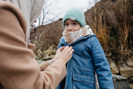 Mother buttoning jacket of kid in cold day in nature