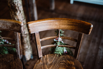 Closeup of two wooden chairs decorated for Christmas with pine leaves and bow
