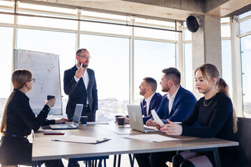 Confident businessman makes a presentation of a new project in the boardroom at a company meeting. Beautiful auditors talk with different partners about the business using a whiteboard and graphs.