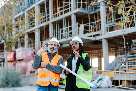 Woman engineer talking with construction worker in front of a building in construction