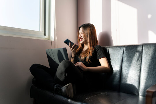 A woman sitting on a sofa in front of the window using a mobile phone