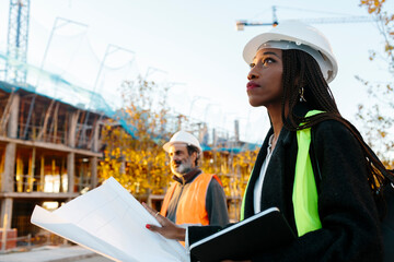 Woman engineer supervising the development of a building in construction checking the plans.