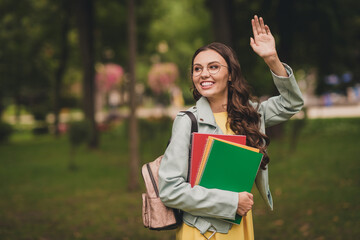 Fototapeta premium Portrait of adorable friendly person carry rucksack copybook look far away arm palm wave have good mood outdoors