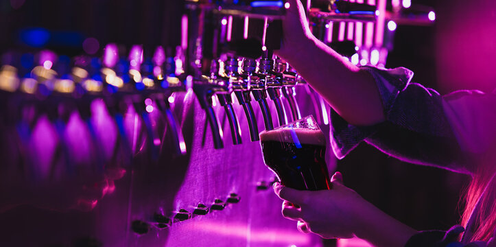 Close-up beer pumps taps in pub or bar in multicolored neon light.