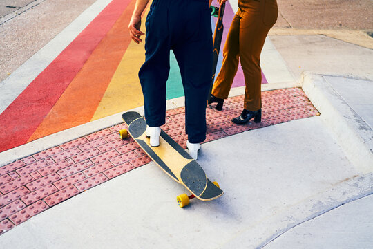 A couple of gay friends waiting to roll over a rainbow flag crosswalk with their hills.