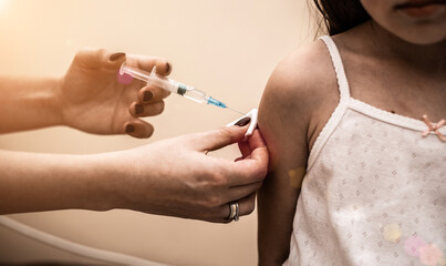 Little girl in the doctor's office is vaccinated. Syringe with vaccine against covid-19 coronavirus, flu, infectious diseases. Injection after clinical trials for human, child. Medicine concept.