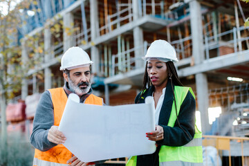 Woman engineer and construction foreman checking blueprints in front of a building in construction.