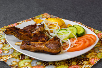 Fried lamb ribs with potatoes and vegetables. Hot meat on a platter.
