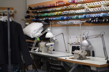 Shot of seamstress workplace. Fashion Design Studio. Sewing Machine and Various Sewing Related Items on the Table, Mannequins Standing, Colorful Fabrics.