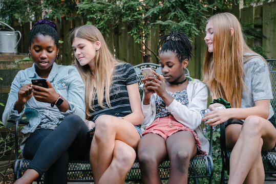 Teen girls sitting on a bench with smartphones