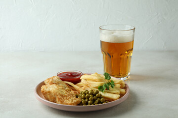 Plate with fried fish and chips, and beer on white textured table