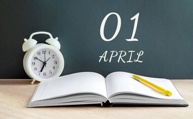 April 01. 01-th day of the month, calendar date. A white alarm clock, an open notebook with blank pages, and a yellow pencil lie on the table. Spring month, the concept of the day of the year