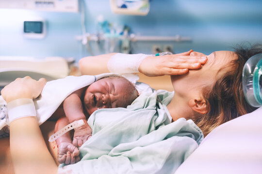 Mother and newborn. Child birth in maternity hospital. Young mom hugging her newborn baby after delivery. Woman giving birth.