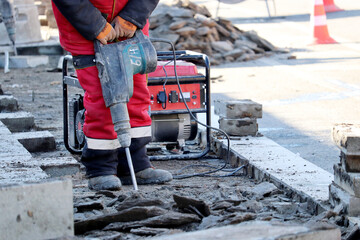 Worker repair the road surface with a jackhammer. Construction work, laying of paving slabs in city