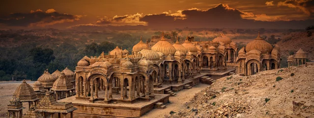 Fotobehang The royal cenotaphs of historic rulers, also known as Jaisalmer Chhatris, at Bada Bagh in Jaisalmer, Rajasthan, India. Cenotaphs made of yellow sandstone at sunset © Konstantin