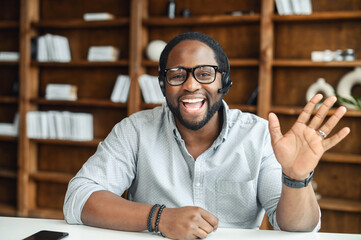 Distance is not a problem. Positive black friendly man in headset practice foreign language communicate online with native speaker using laptop, remote student wave hand greet prof by video call