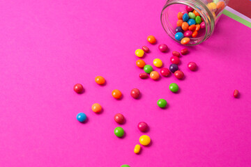 colorful candies poured from a glass jar on a colored background