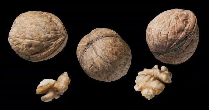 Three walnuts and two shelled walnuts rotate slowly on a black background. 