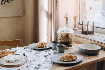 the croissant lies in a blue plate on the kitchen table with cups of tea for two. oatmeal cookies in glass vintage jar