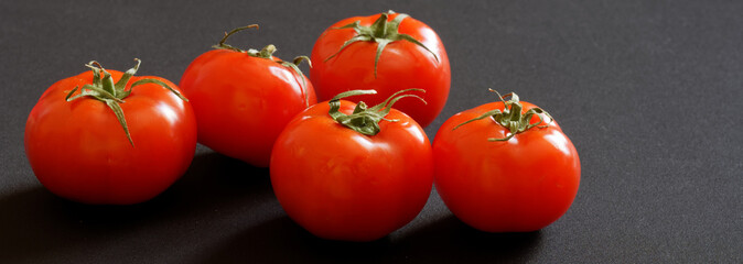 Five fresh red tomatoes lie on a gray background. Banner. Free space for an inscription.