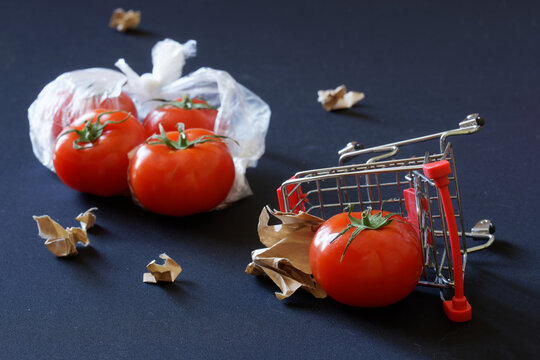 Red tomatoes, overturned supermarket carts and torn pieces of paper are scattered against a dark background. Concept of trade problems, farm strikes and anti-globalization