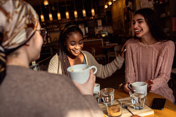 Three young multiethnic female friends spending time together at a coffee shop.