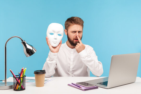 You Are Liar! Bearded Man Office Employee Touching Nose With Finger Holding White Face Mask In Hand, Blaming In Lie, Suspecting Of Dishonest. Indoor Studio Shot Isolated On Blue Background