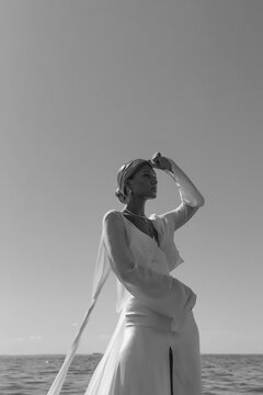A blonde haired woman standing on the beach wearing a long bridal gown