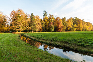 Autumn public park with creek, meadow and colorful trees
