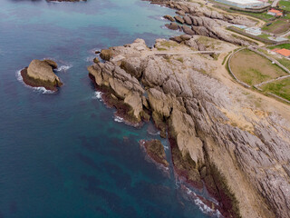 Aerial view of sea waves hitting rocks on the beach with turquoise sea water.