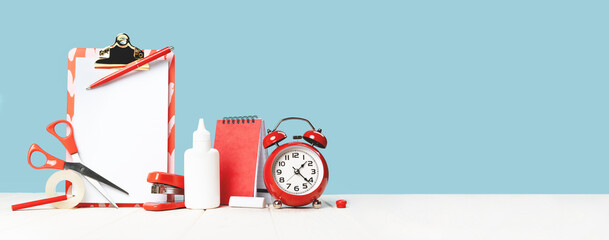 Group of office and school red stationery on desk blue background. Alarm clock. Banner for back to...