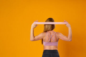 happy attractive pregnant woman in sports clothes does exercises with an elastic sports elastic band on yellow background, studio. health during pregnancy. sports at home. Motherhood, active pregnancy