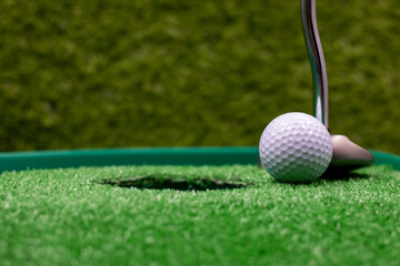 Golf ball and putter for putting on green grass next to hole