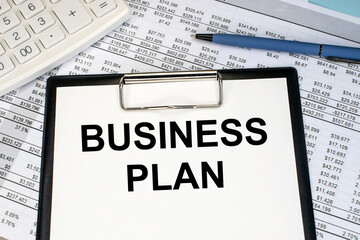 On the financial document near the calculator is a stationery tablet on which the inscription business plan.