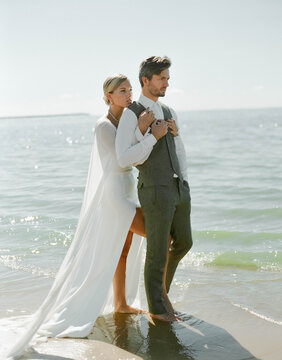 A just married couple standing on a beach, enjoying their time and the bride gives a hug to the groom