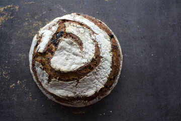 Long-fermented sourdough loaf top view photo. Beautiful round whole grain bread on a table. Still life food.  
Gray textured background with copy space.  