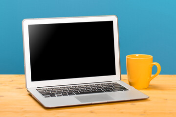 Laptop with blank screen for product display and cup of coffee on wooden table