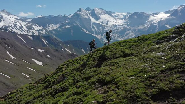 Two young hikers (a couple) walking up a mountain in Austria in summer, with scenic snow covered mountains on the background