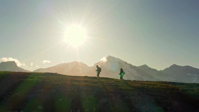 Silhouettes of two young hikers (a couple) walking on a mountain ridge in Austria in summer