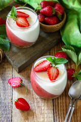 Panna cotta with strawberry jelly and fresh strawberries on a rustic wooden table, summer italian dessert, home cooking.