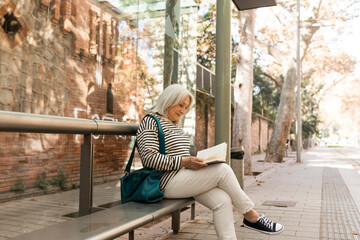 mature woman waiting for the tram sitting reading a book