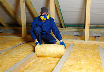 Worker thermally insulating house attic with glass wool