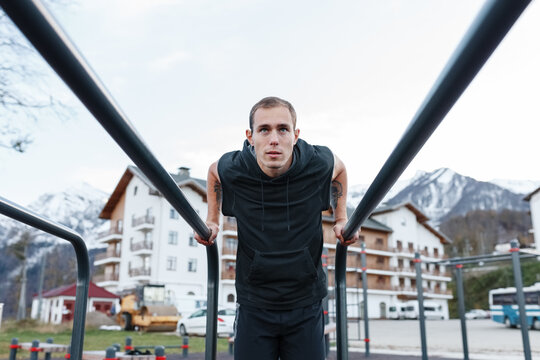 Determined athlete exercising on bars in town