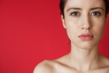 Close up photo of a caucasian woman with freckles looking at camera while posing on a red wall with...