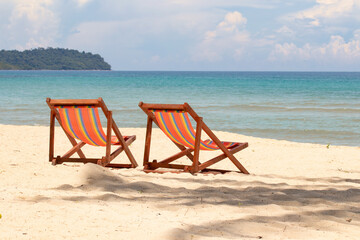 Sunbeds, deckchairs on the beach in front of tropical island.