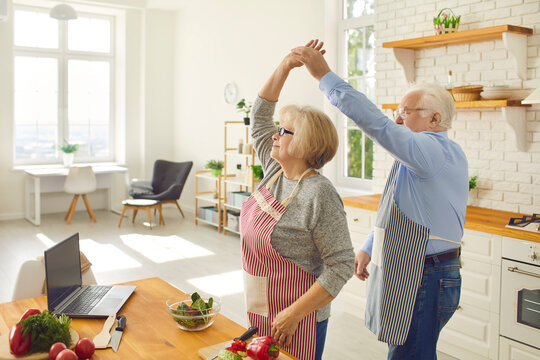 Happy Senior Couple Having Fun While Cooking Healthy Vegetarian Meal In The Kitchen Of Their Studio Apartment. Senior Citizens Leading Active Lifestyle, Enjoying Life, Spending Time Together At Home