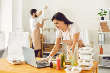 Healthy food delivery. Woman and a male colleague form an order for a food delivery service that they receive through a website. Man in the background completes the customers order.