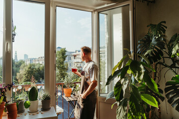 A man on a balcony among green indoor plants.